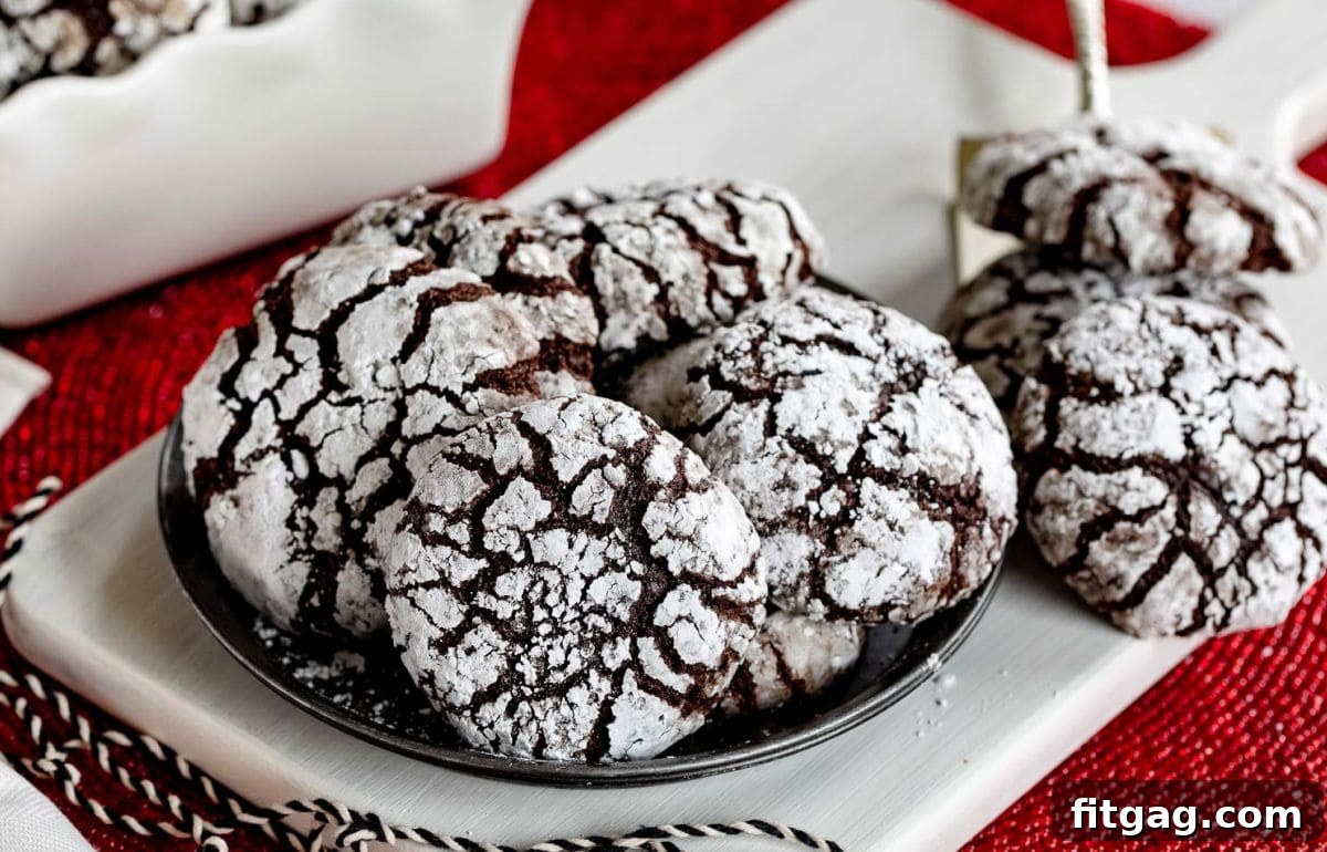 Plate of chocolate crinkle cookies with more cookies sitting off to the side and a few more in a white ceramic container. Red placemat sitting underneath.