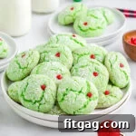 grinch cake mix cookies with red heart sprinkles sitting on white plate with milk jars in the background and Christmas ornaments scattered about.