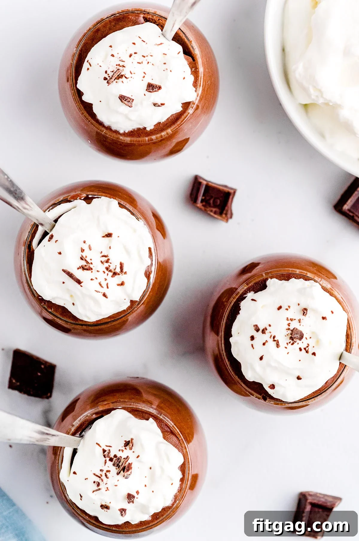 Four glasses brimming with homemade chocolate mousse, elegantly topped with whipped cream and delicate chocolate shavings, invitingly ready for enjoyment.