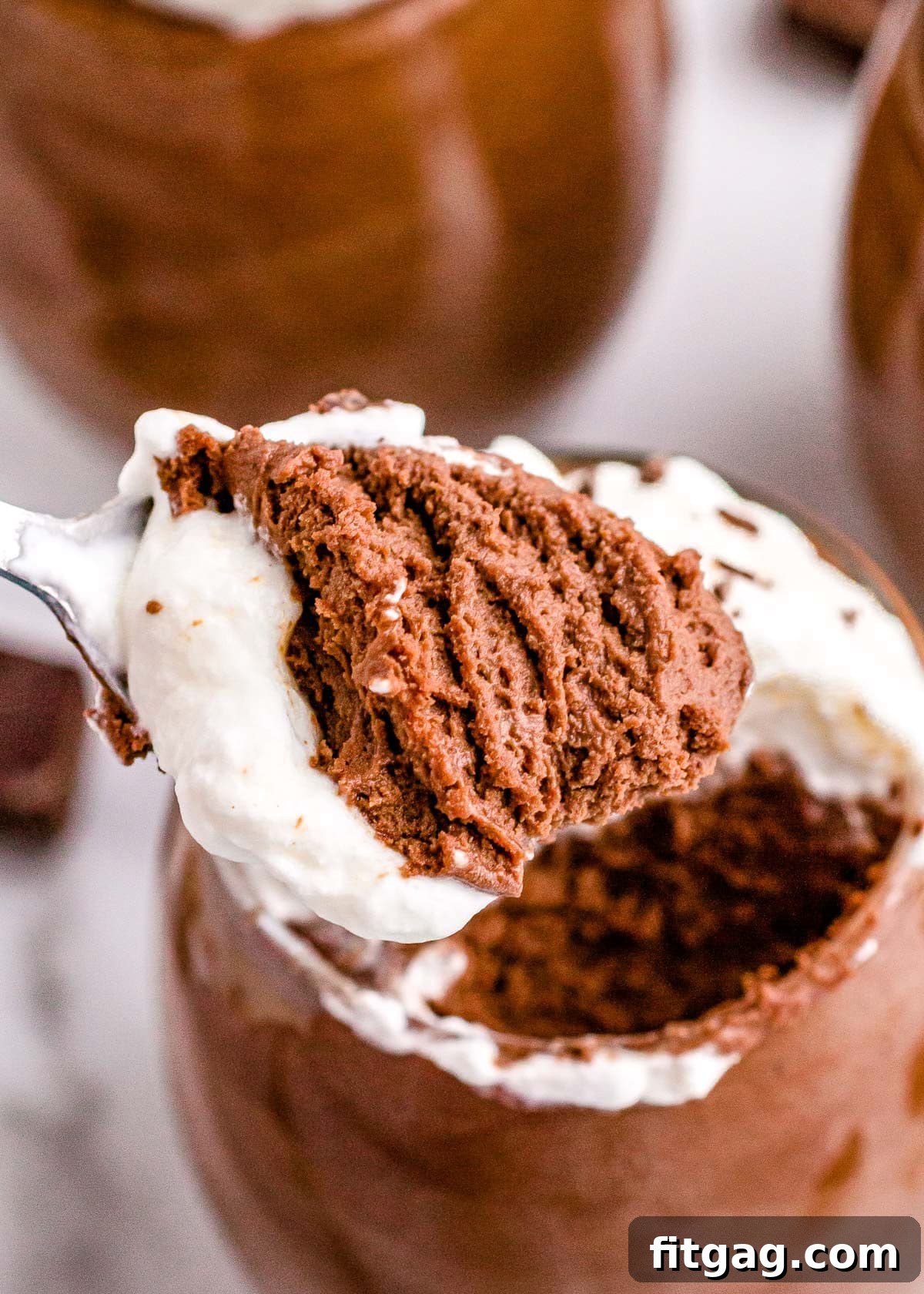 A spoonful of decadent chocolate mousse held just above the serving glass, showcasing its airy, luscious texture.