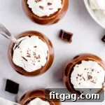 top down view of four glasses with chocolate mousse in them topped with whipped cream and chocolate shavings ready to be eaten.