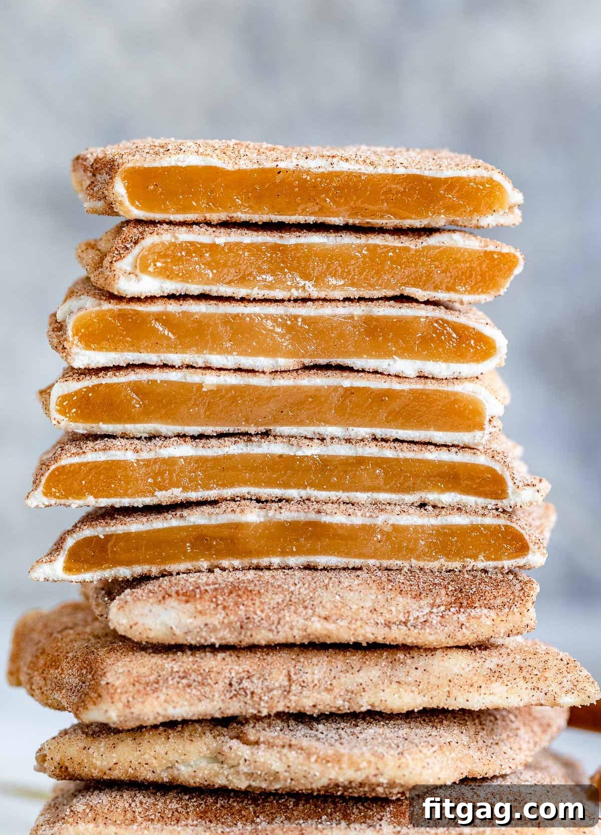 Square churro toffee pieces stacked, showcasing the golden toffee, white chocolate layer, and cinnamon sugar coating.