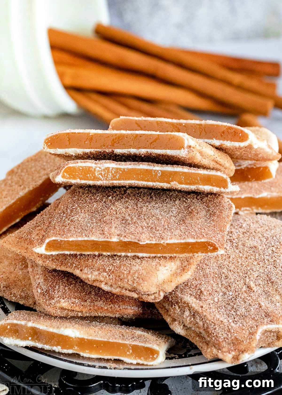 Pile of churro toffee pieces on a black and white plate with cinnamon sticks in the background.
