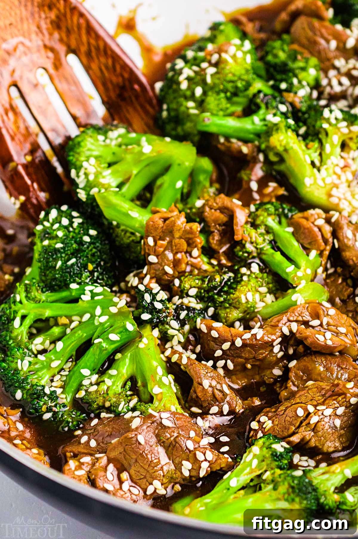 Restaurant-Style Beef and Broccoli Stir-fry 2 A vibrant Beef and Broccoli stir fry, generously topped with white sesame seeds, presented in a pristine white skillet alongside a wooden serving spoon, ready to be enjoyed. The rich colors of the beef, green broccoli, and golden sauce promise a delicious meal.