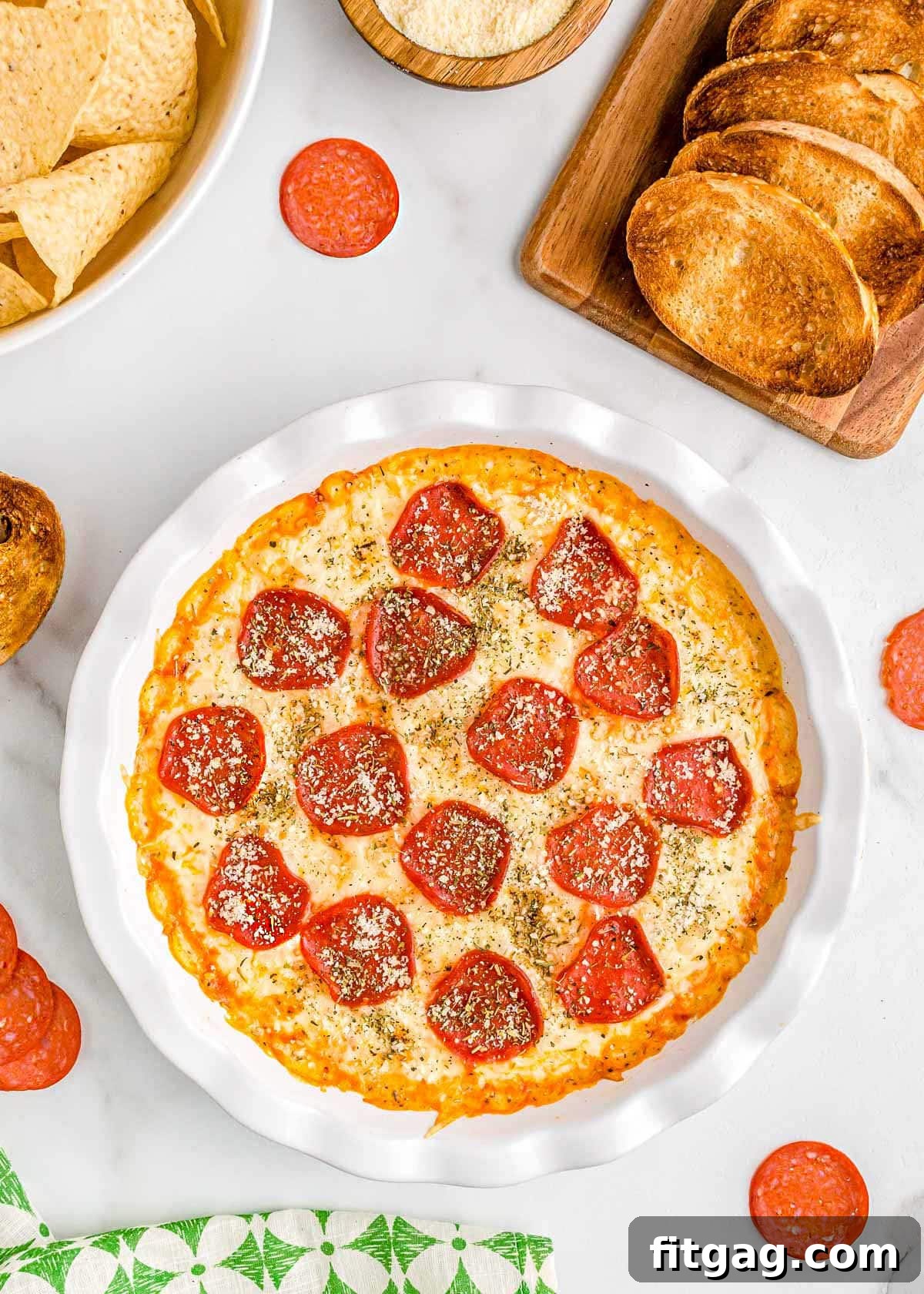 Baked Cheesy Pizza Dip 2 Bubbly pepperoni pizza dip baked in a white pie dish, garnished with Parmesan cheese, ready to be served with toasted baguette slices and chips.