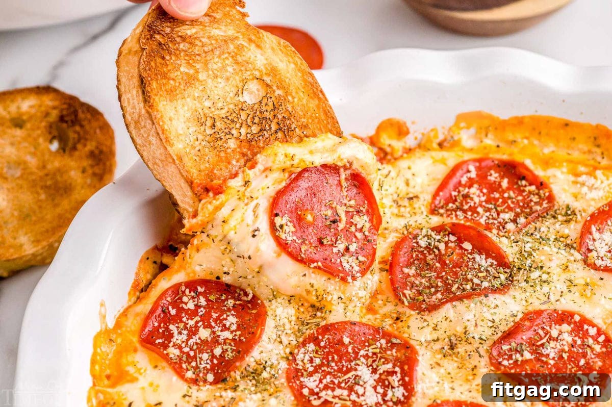 Baked Cheesy Pizza Dip 3 A slice of golden garlic bread being dipped into a hot, cheesy pizza dip topped generously with pepperoni slices.