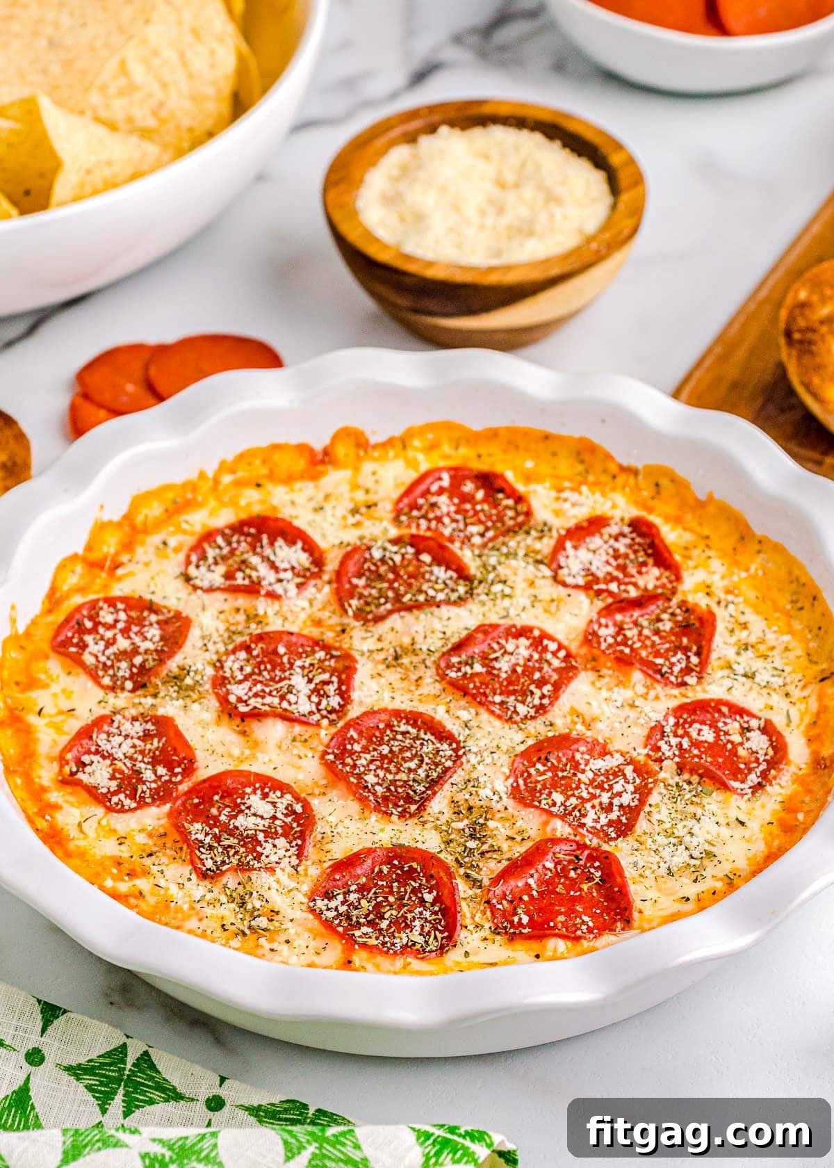Baked Cheesy Pizza Dip 6 A top-down view of the beautifully baked pepperoni pizza dip, resting in a white pie dish, ready to be devoured. Toasted baguettes and chips are arranged on the side.
