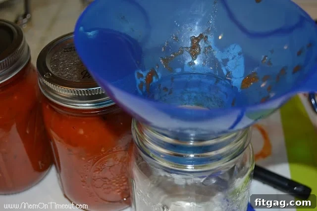 Filling hot, sterilized canning jars with fresh homemade pasta sauce using a funnel, preparing them for the water bath.
