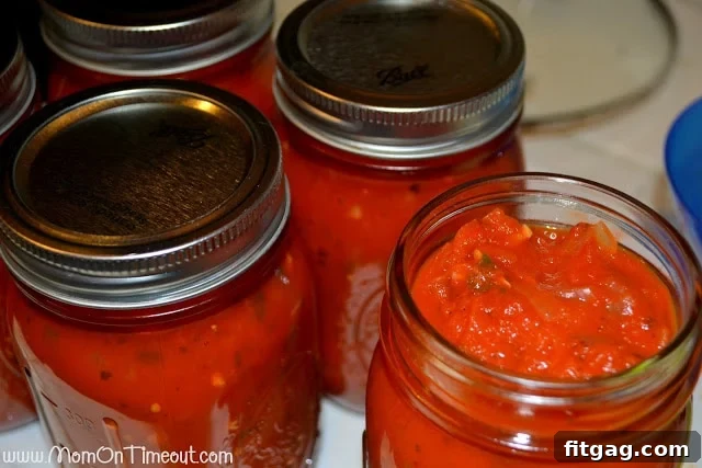 Canning jars filled with homemade pasta sauce being processed in a boiling water bath for safe preservation.