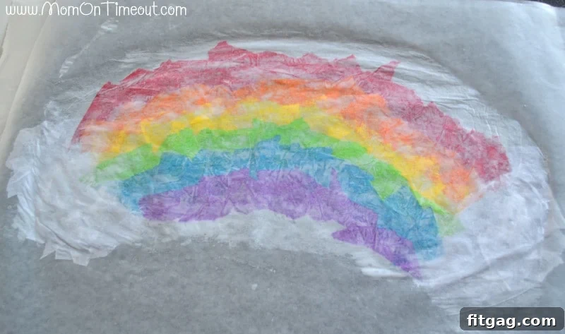 Sparkling Rainbow Suncatchers 7 Hands carefully placing a second glue-covered waxed paper sheet on top of the tissue paper rainbow, sealing the craft.