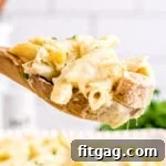 A wooden spoonful of creamy chicken alfredo bake held above the baking dish, ready to be served.