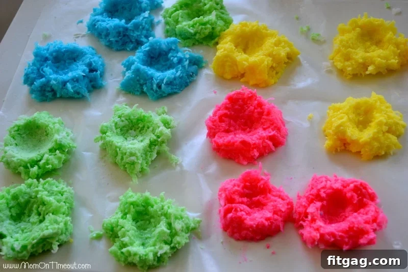 Close-up shot showing a thumb pressing down to create a perfect indentation in a colorful coconut nest mixture set on waxed paper.