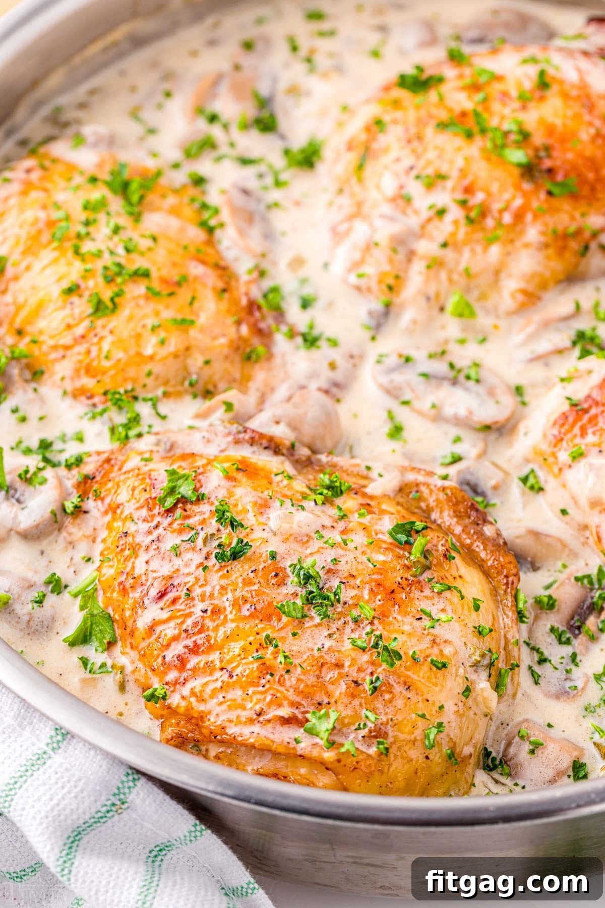 Tender Chicken in Velvety Sauce 2 skillet with four chicken thighs browned and simmering in a white wine mushroom sauce. A sprinkling of parsley over the top provides a nice contrast.