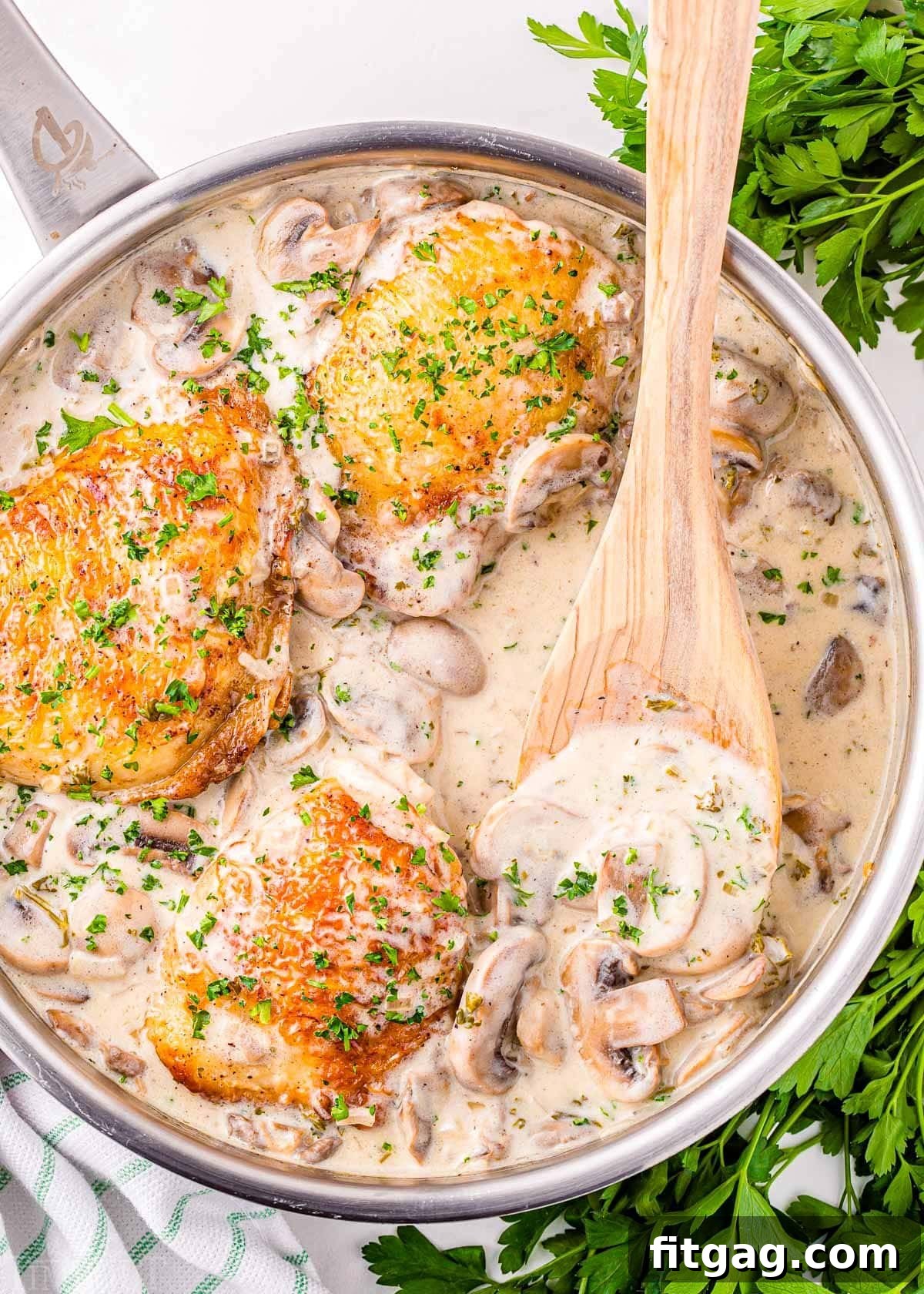 Creamy Chicken Comfort 4 A top-down view of the rustic skillet, showcasing the simmering chicken fricassee. A wooden spoon, laden with the creamy white wine mushroom sauce, is poised above the tender chicken, ready to serve.