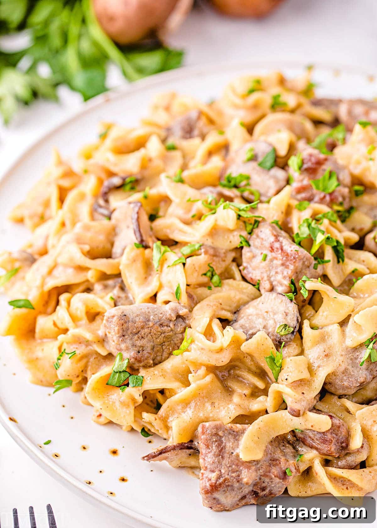 Close up image of Instant Pot Beef Stroganoff plated on a white dinner plate, garnished with fresh parsley. The tender beef, creamy sauce, and noodles are perfectly visible, inviting a delicious meal.