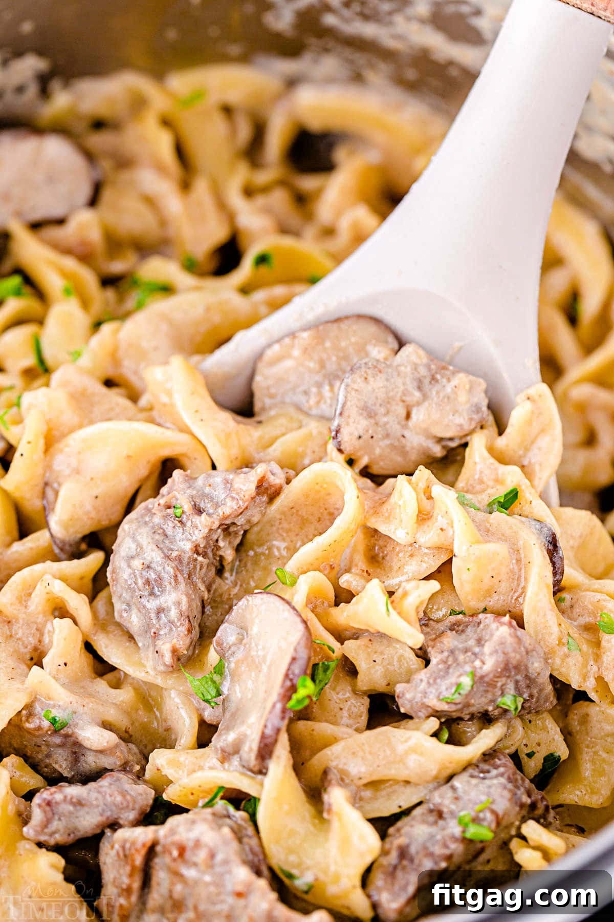 Close up look of a spoonful of creamy beef stroganoff still in the Instant Pot, highlighting the tender beef pieces, savory mushrooms, and thick, rich sauce.