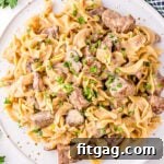 Top down view of a white plate filled with beef stroganoff, garnished with fresh parsley, emphasizing the creamy sauce and tender ingredients.