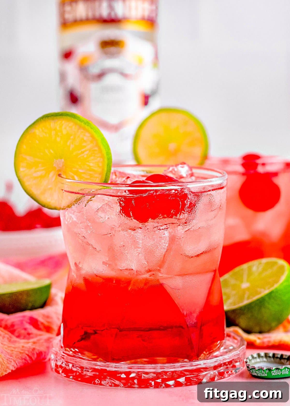 two dirty shirley temple cocktails garnished with lime and marschino cherries with the bottle of vodka in the background.
