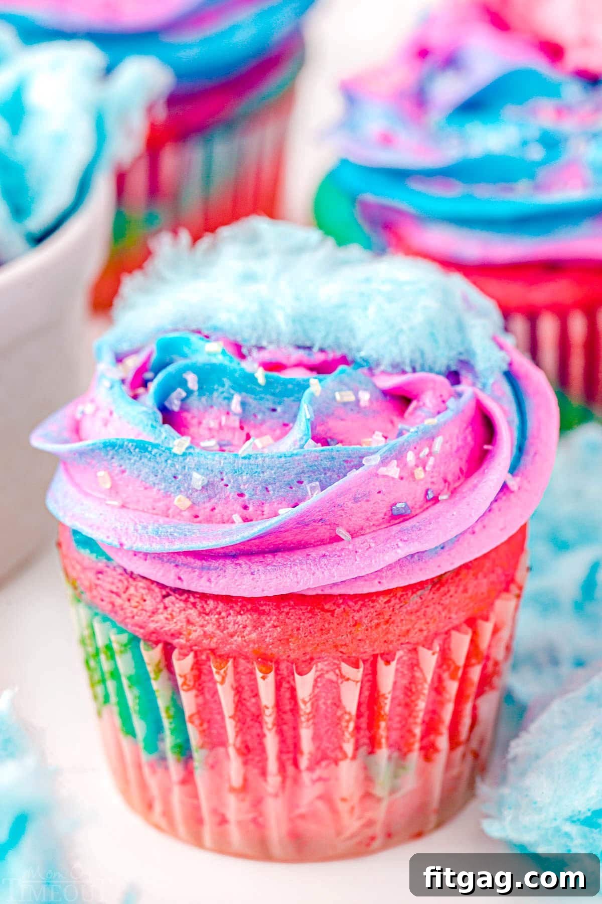 A close-up view of a swirled cupcake featuring vibrant blue and pink frosting, topped with a small, delicate piece of cotton candy.