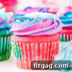 cotton candy cupcakes decorated with pink and blue frosting and topped with cotton candy ready to be enjoyed. Bits of cotton candy are scattered around the cupcakes as well.