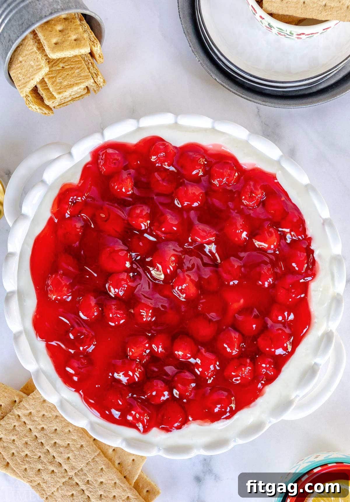 An overhead view of a white ceramic pie plate overflowing with vibrant cherry cheesecake dip, surrounded by an inviting array of graham crackers for dipping.