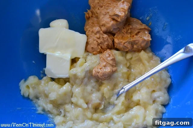 Mashed bananas thoroughly mixed with softened butter and chunky peanut butter in a blue mixing bowl, forming a creamy base.