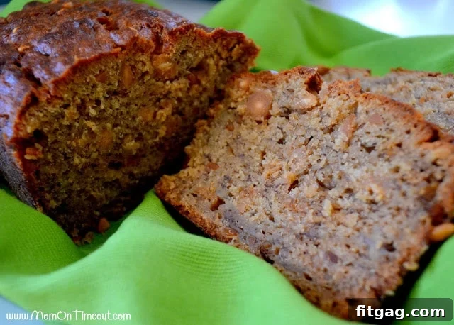 A beautifully baked loaf of Peanut Butter Banana Bread, with two slices already cut, resting on a soft green towel on a wooden surface.