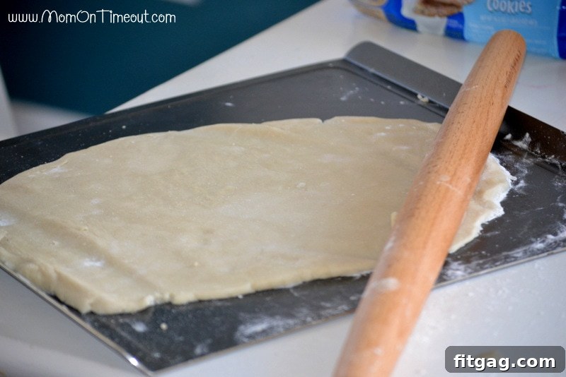 Confetti Sugar Cookie Bark 6 Hands rolling out refrigerated sugar cookie dough on parchment paper, creating a perfect base for the Rainbow Sugar Cookie Bark. A key step for this easy and fun recipe.