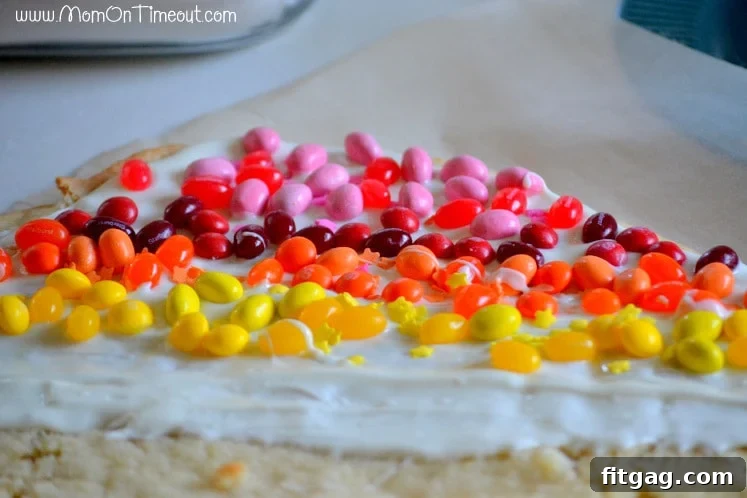 Confetti Sugar Cookie Bark 7 Adding individual candies to the melted vanilla coating on a baked sugar cookie, carefully arranging them to form vibrant rainbow stripes for the cookie bark.