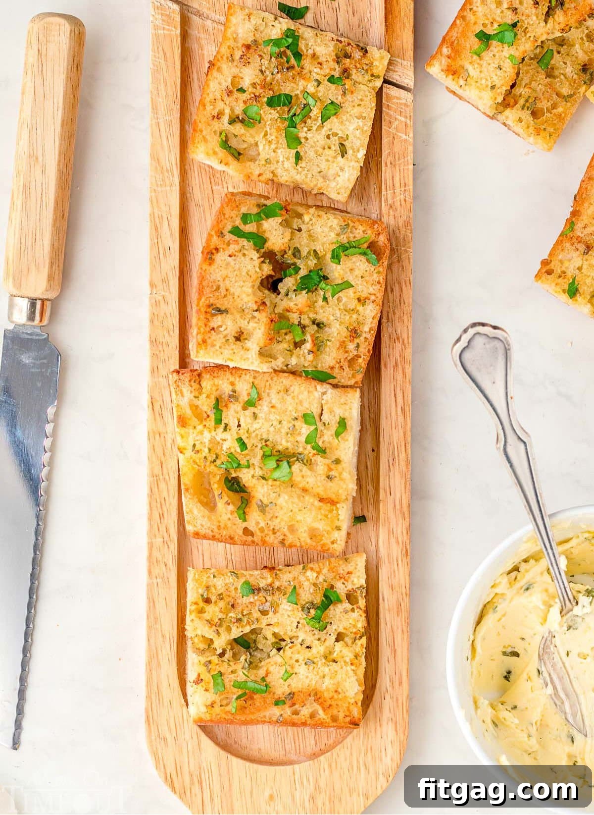 Crispy Air Fryer Garlic Bread 3 wood board with garlic bread cut into pieces on it. bowl of garlic butter off to the side with more pieces of garlic bread and a knife on the other side.