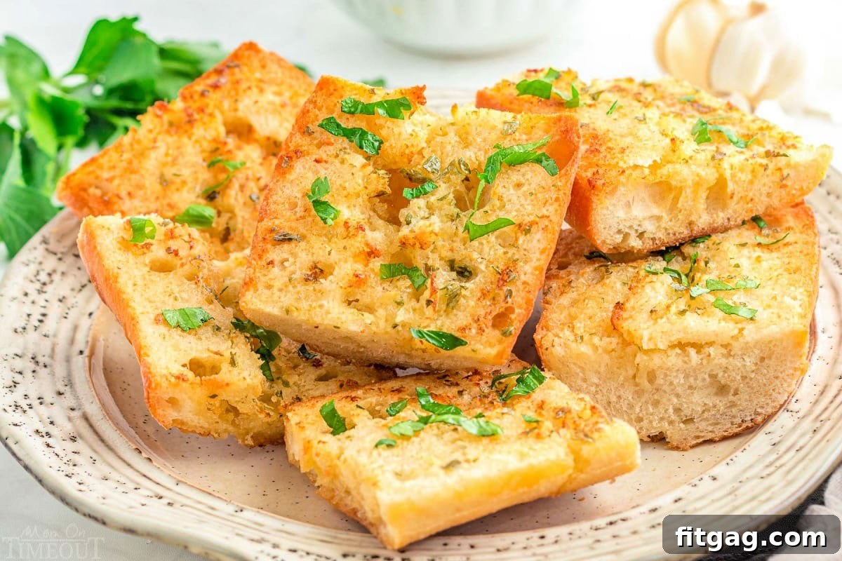 Crispy Air Fryer Garlic Bread 7 wide shot of garlic bread sliced and ready to serve off a white plate. fresh parsley garnish on the bread.