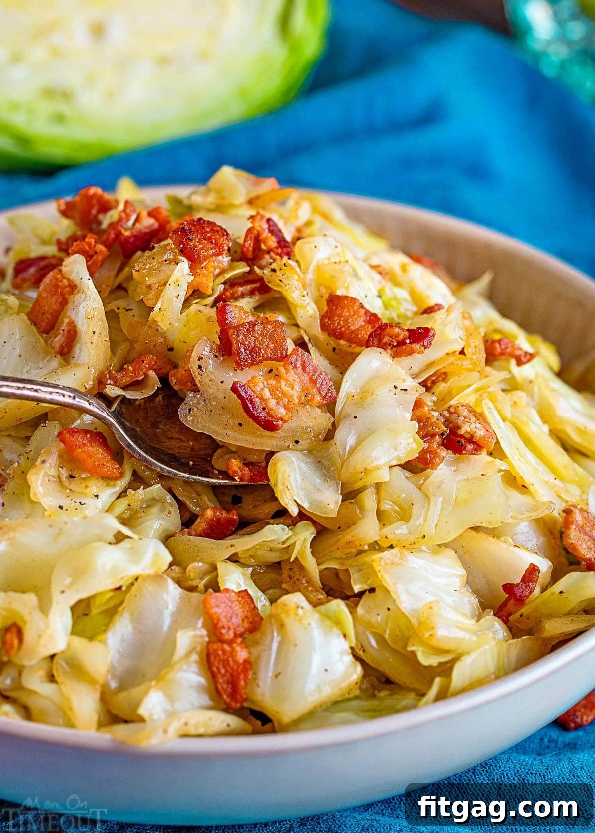 Golden Fried Cabbage 6 A white bowl holds a generous serving of our delicious fried cabbage recipe, with a spoon nestled into the food, poised for a savory bite. The textures of the tender cabbage and crispy bacon are inviting.