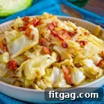 A shallow bowl filled with fried cabbage made with bacon, onion and garlic. The bowl is sitting on a bright teal napkin and half a head of cabbage is in the background.