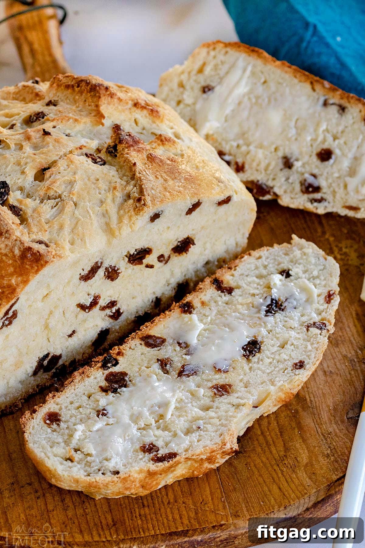 A perfectly baked loaf of Irish Soda Bread, with one slice cut and buttered, resting on a rustic round wooden board. The top-down view highlights its golden crust and tender interior.