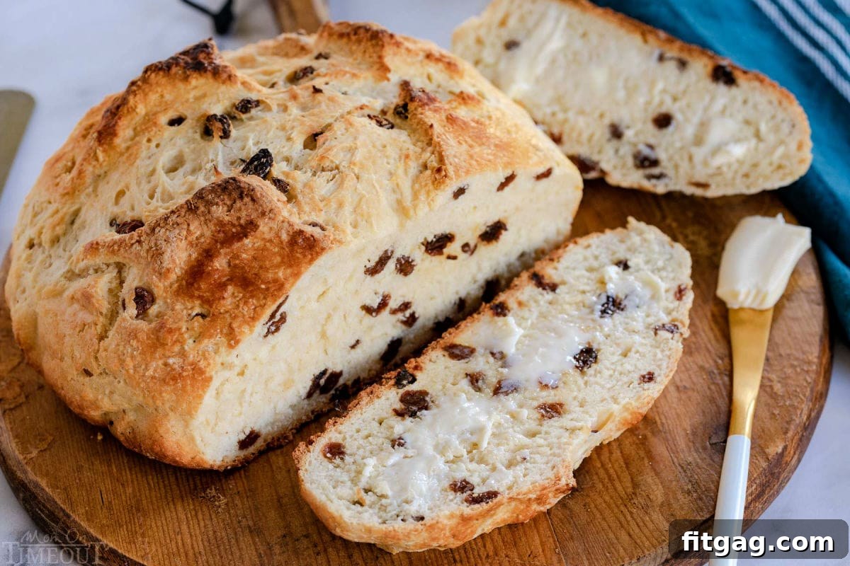 A top-down view of a freshly baked loaf of Irish Soda Bread, with one slice cut and buttered, presented on a rustic round wooden board, ready for enjoyment.