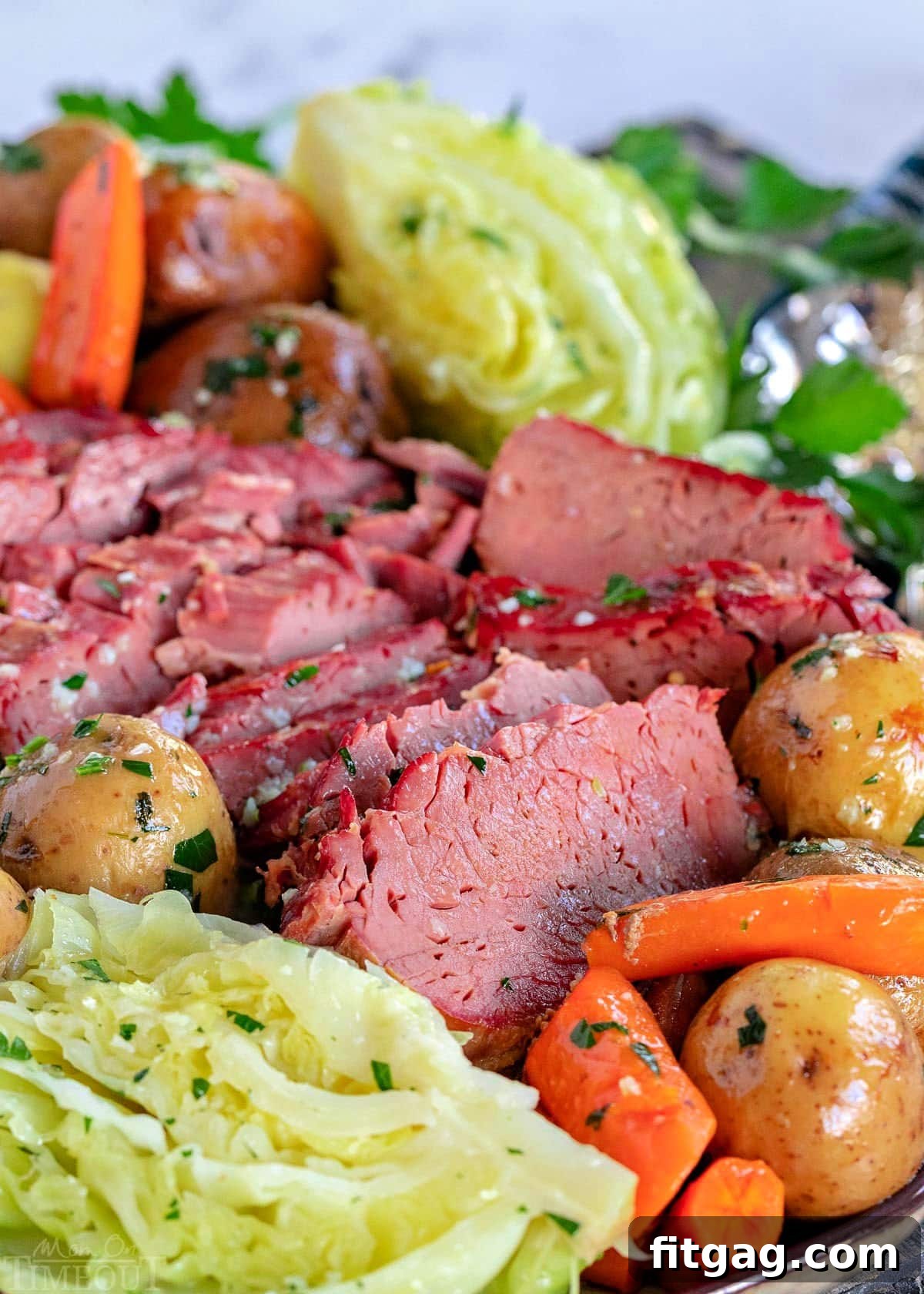 Tender Slow Cooker Corned Beef and Cabbage 3 close up look at slices of slow cooker corned beef and cabbage wedges plus potatoes and carrots on a serving platter brushed with garlic herb butter.