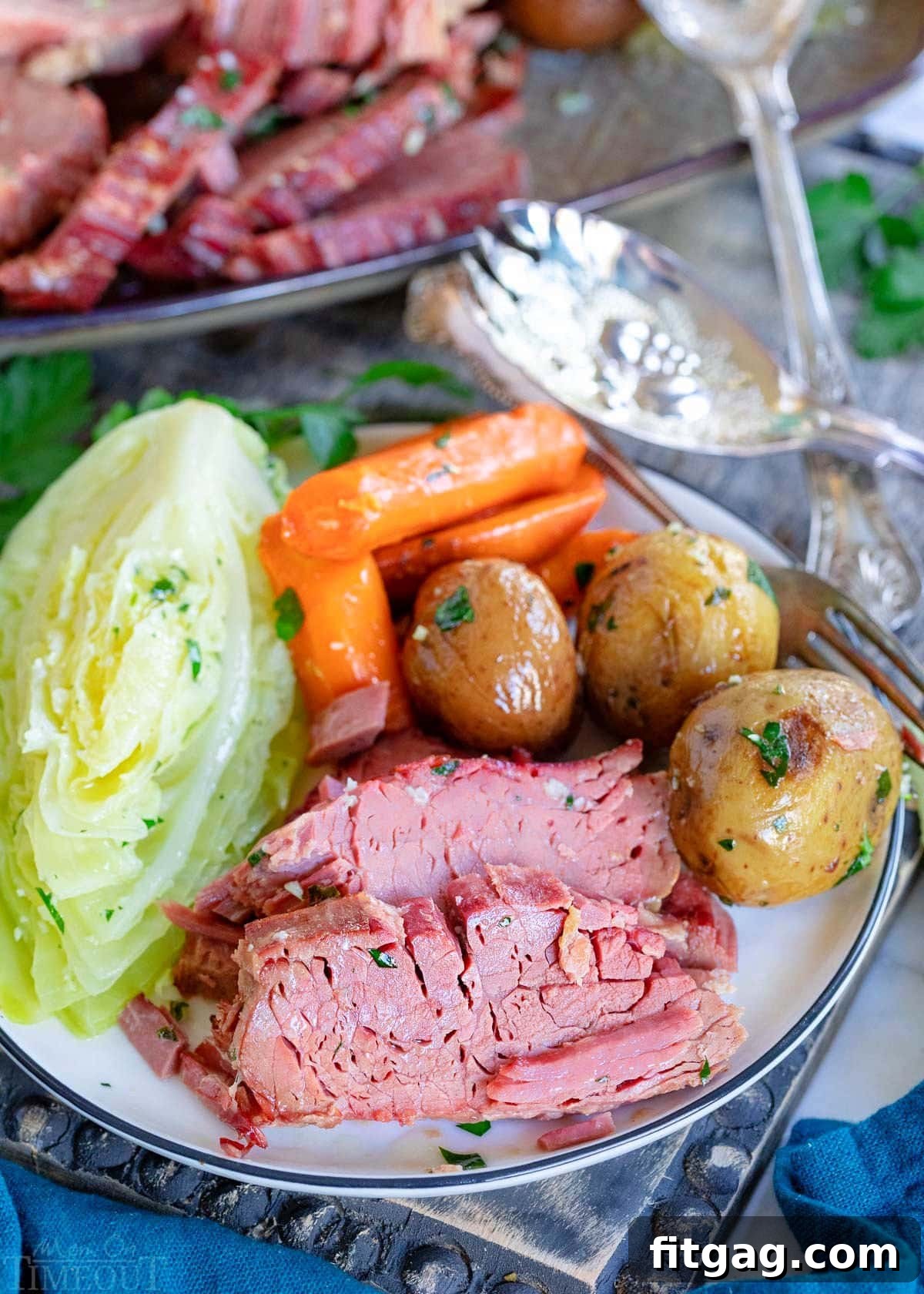 Tender Slow Cooker Corned Beef and Cabbage 6 plate with a few slices of corned beef and cabbage, potatoes and carrots sitting on a gray wood board with serving plate in background.