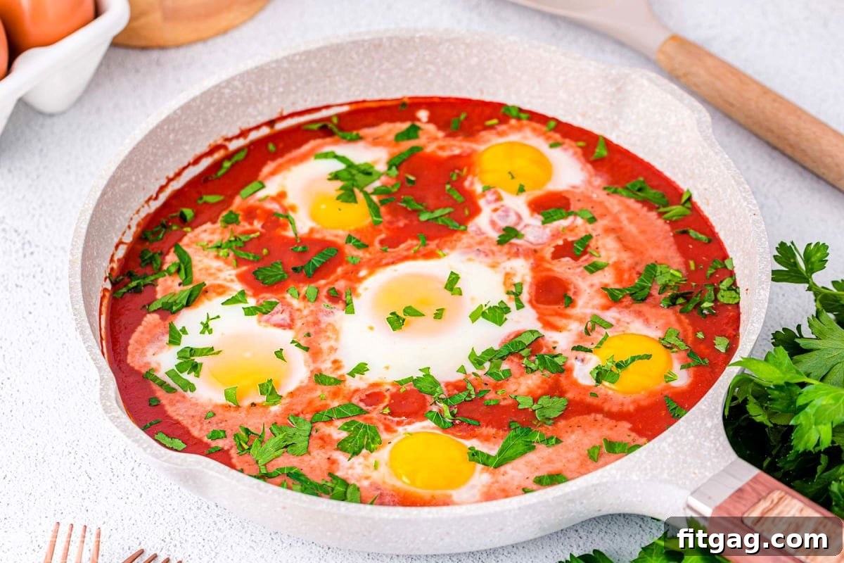 Wide shot of a light-colored skillet containing six eggs perfectly poached in a vibrant red tomato sauce, generously topped with fresh parsley.