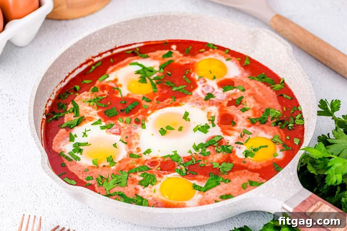 wide shot of light colored skillet with six eggs poached in tomato sacue and topped with fresh parsley.
