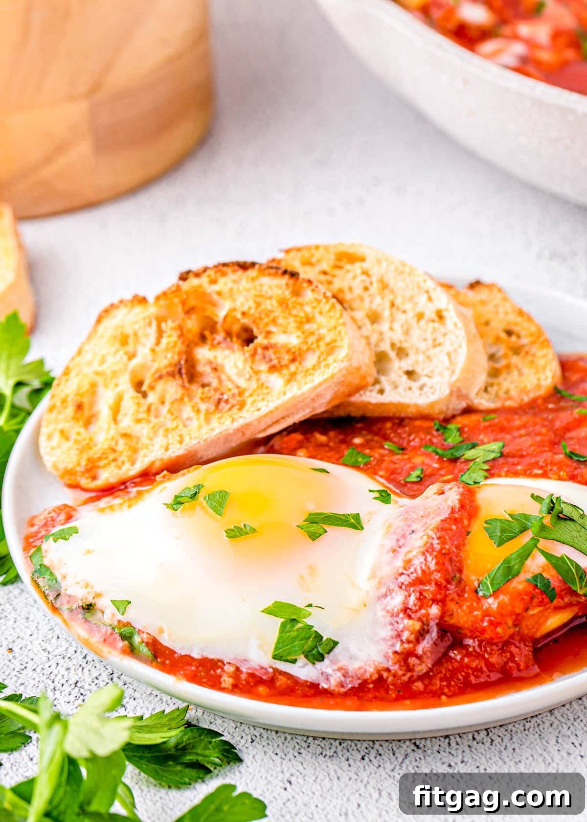 eggs in purgatory plated with extra sauce and nicely toasted crusty bread. The dish is topped with chopped parsley.