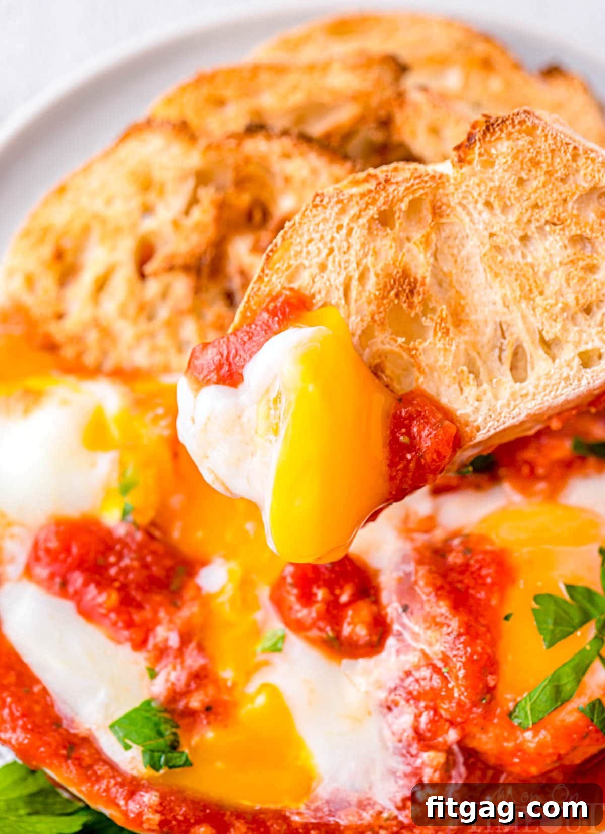Piece of toasted crusty bread being dipped into the runny yolk of a poached egg in a skillet of Eggs in Purgatory.