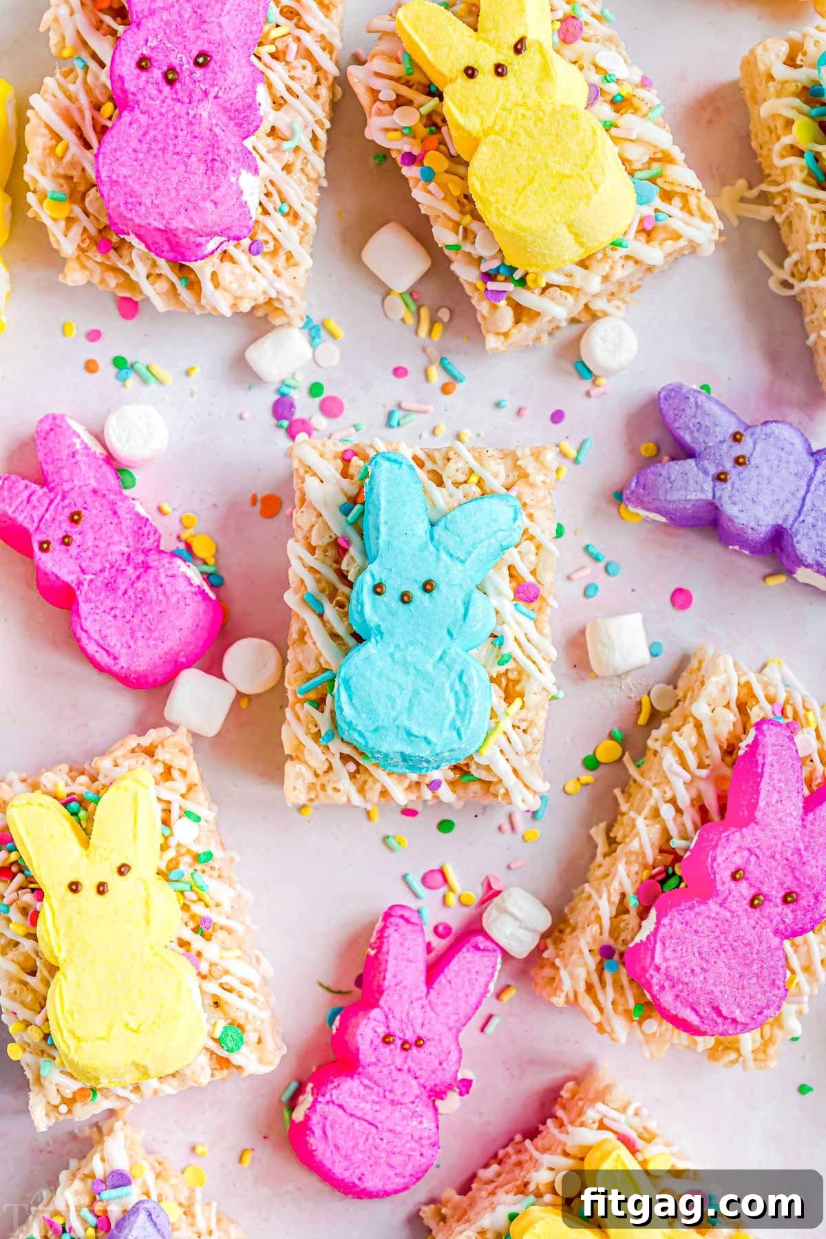 Gooey Peeps Cereal Bars 2 Delightful Easter Rice Krispie Treats decorated with white candy melts and colorful sprinkles, each topped with a different colored Peep. A top-down view of the treats arranged on parchment paper, ready for a festive celebration.