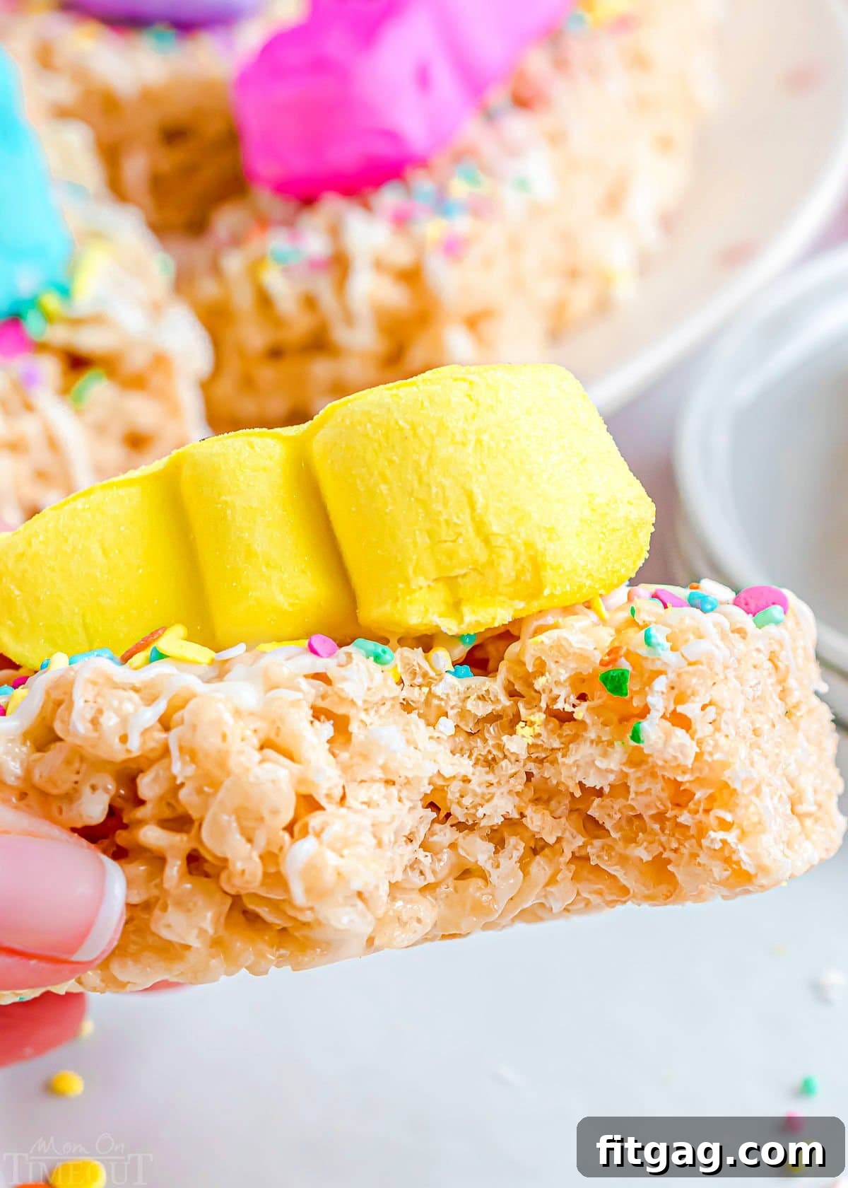Gooey Peeps Cereal Bars 7 A close-up of a Peeps Rice Krispie Treat held up with a bite taken out, showing the chewy interior and a yellow Peep on top.