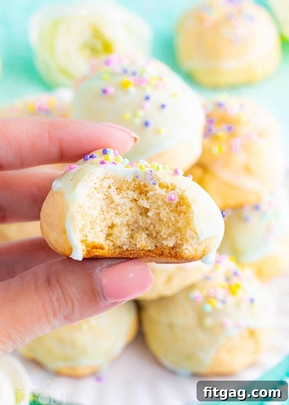 Sweet Italian Easter Cookie Delights 3 A close-up of an Italian cookie held up, revealing a bite taken out, with more pastel-glazed cookies visible on a plate in the soft-focus background.