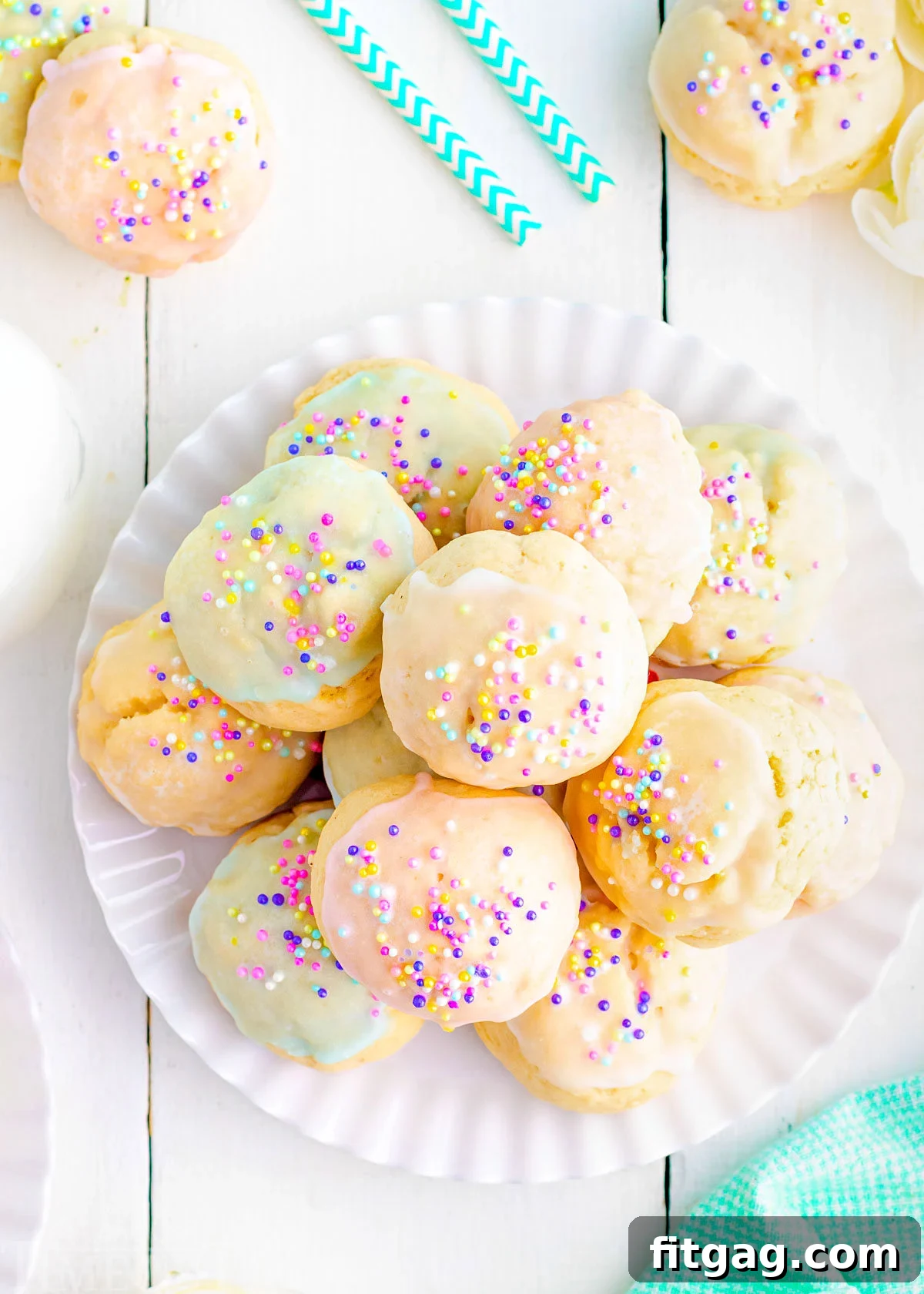 Sweet Italian Easter Cookie Delights 4 A top-down view of a white plate generously piled high with various Italian Easter cookies, all adorned with pastel glazes and colorful sprinkles, set against a pristine white wood backdrop.