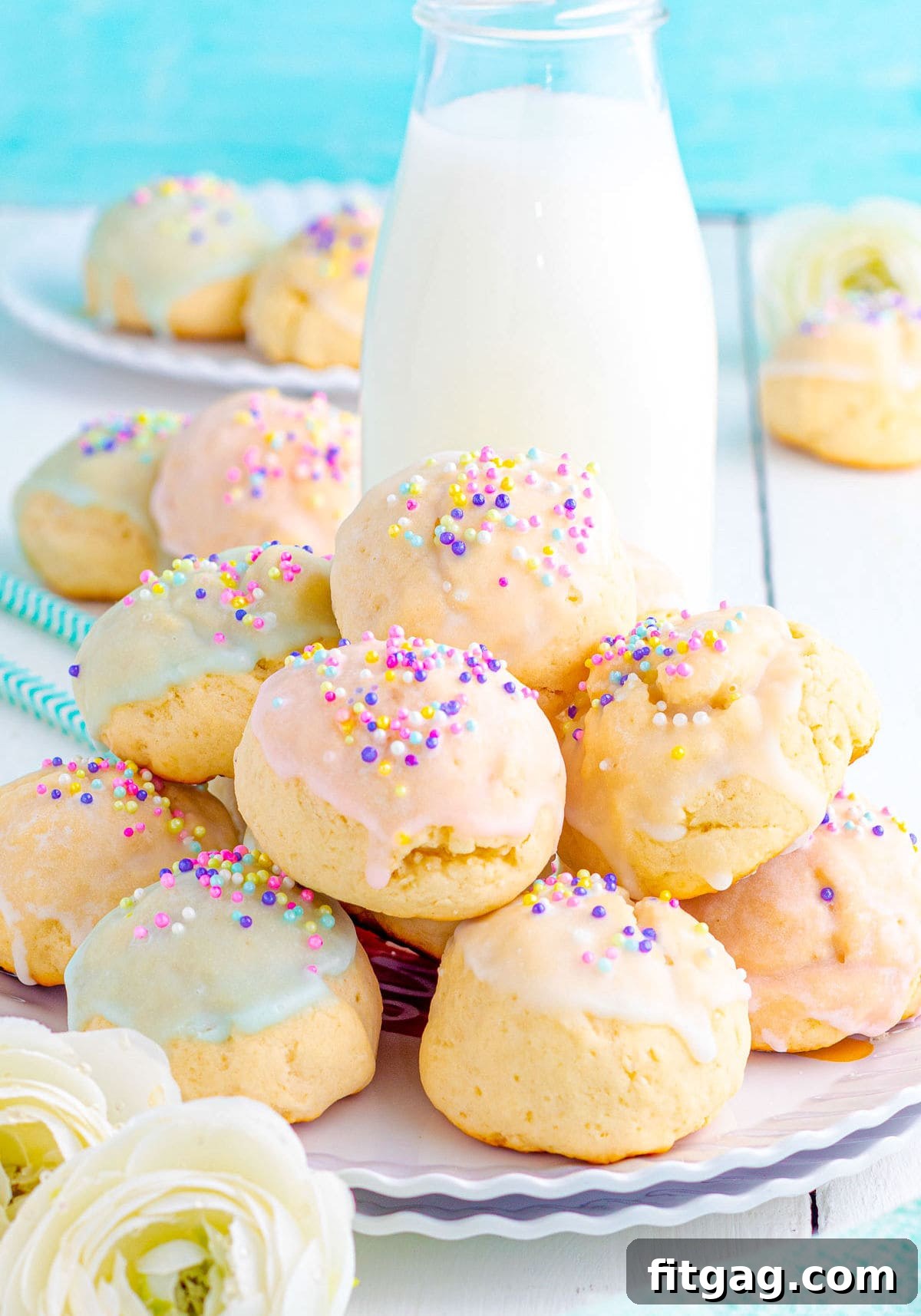 Sweet Italian Easter Cookie Delights 7 A charming plate of Italian Easter Cookies, beautifully decorated with pastel glazes and sprinkles, sits in front of a jug of milk. An aqua background and more cookies blurred in the distance complete the festive scene.