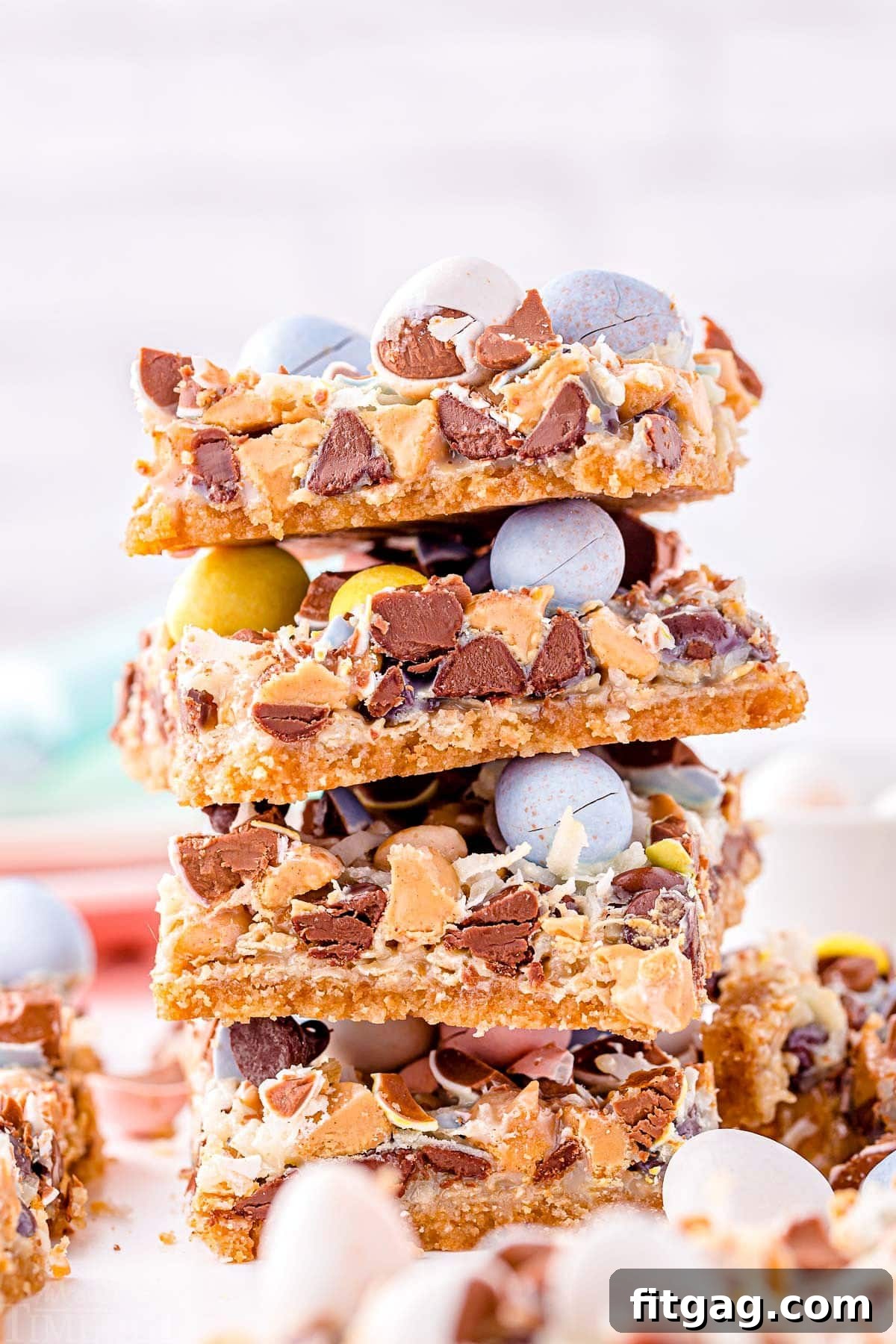 Whimsical Easter Magic Bars 2 magic cookie bars topped with cadbury easter eggs stacked four high on a white surface.