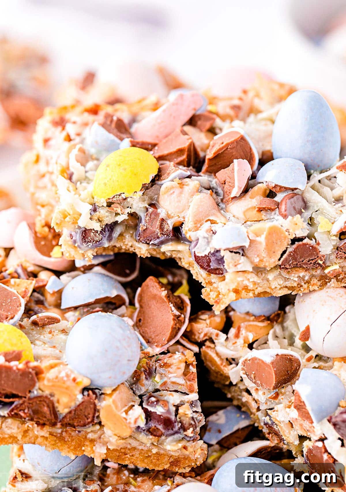 Whimsical Easter Magic Bars 3 cadbury eggs seven layer bars stacked on a plate with the top bar having a bite taken.