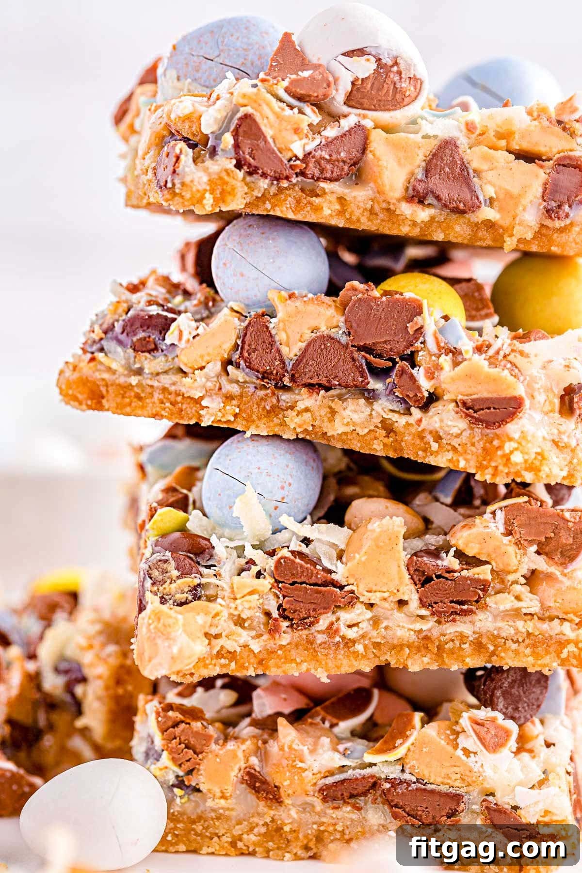 Whimsical Easter Magic Bars 6 close up look at magic cookie bars topped with cadbury easter eggs stacked four high on a white surface.
