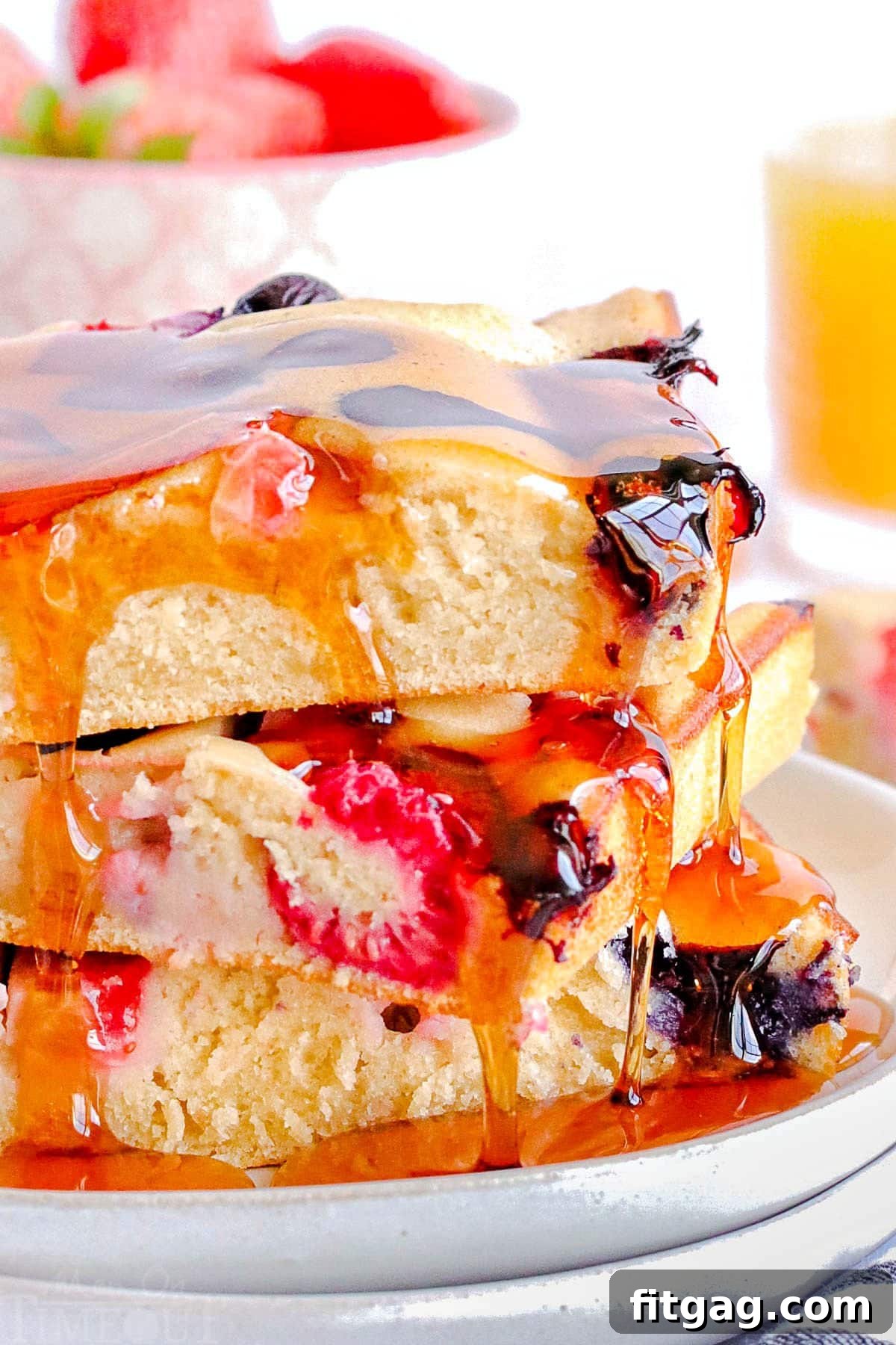 A close-up shot captures the luscious cascade of golden maple syrup dripping slowly off the side of three perfectly stacked fluffy pancakes, highlighting their soft, inviting texture.
